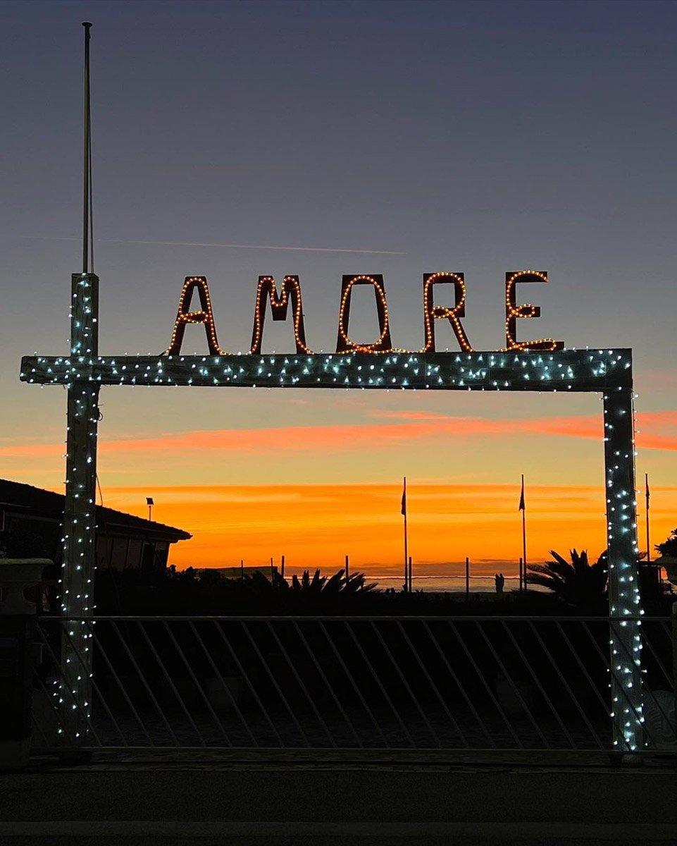 A sign reading AMORE near a Viareggio beach during sunset in winter.